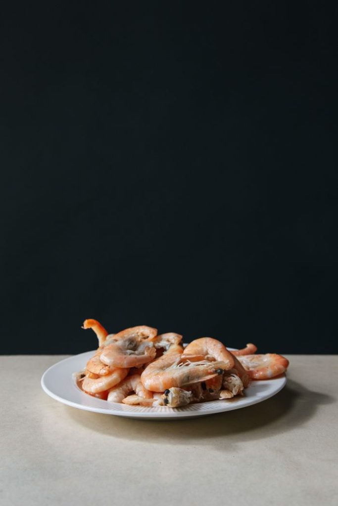 A minimalist still life of fresh shrimps served on a white plate against a dark backdrop.